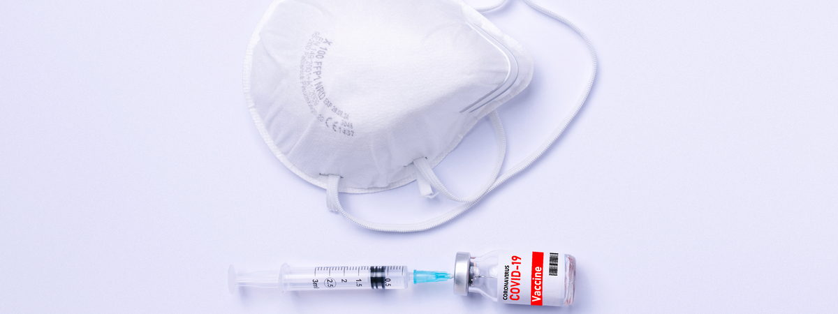 N95, FFP2 medical mask to prevent infection with coronavirus COVID-19. Syringe and ampoule with a vaccine. White background and empty space.